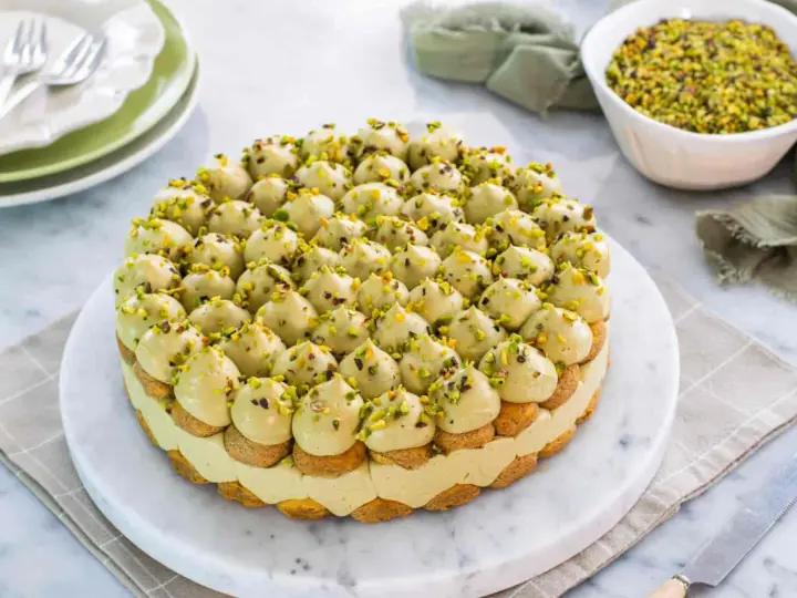 Torta rotonda con tante piccole meringhe verdi, guarnite con granella di pistacchio. Un delizioso tiramisù al pistacchio pronto per essere gustato.