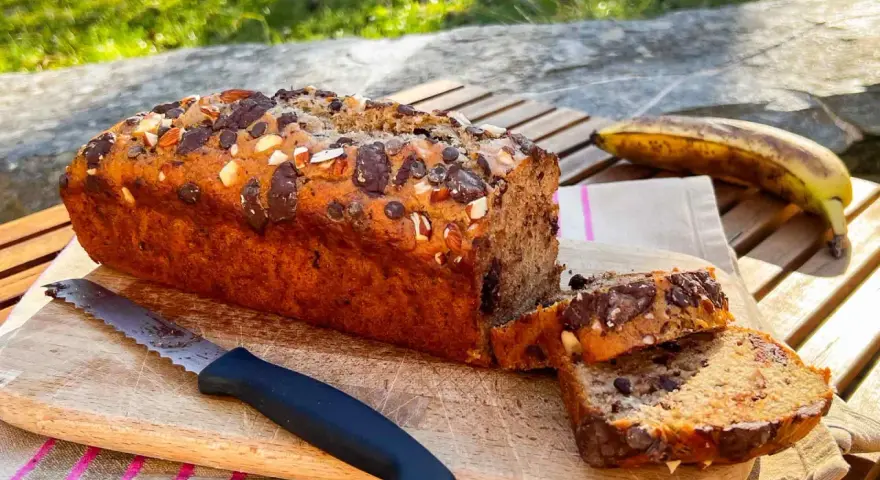 Delizioso banana bread vegano con gocce di cioccolato e mandorle, pronto per essere gustato all'aperto.