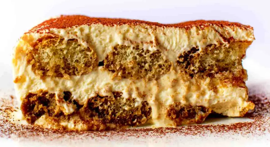 Una fetta di tiramisù, con strati di savoiardi inzuppati e crema al mascarpone, spolverata di cacao. La ricetta perfetta per un dolce indimenticabile.