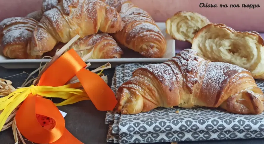 Croissant dorati e soffici, dolci lievitati spolverati di zucchero a velo, pronti per una colazione speciale.