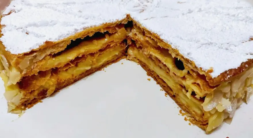 Un delizioso millefoglie alla crema, con strati croccanti di pasta sfoglia e una ricca crema pasticcera, spolverato di zucchero a velo e mandorle.