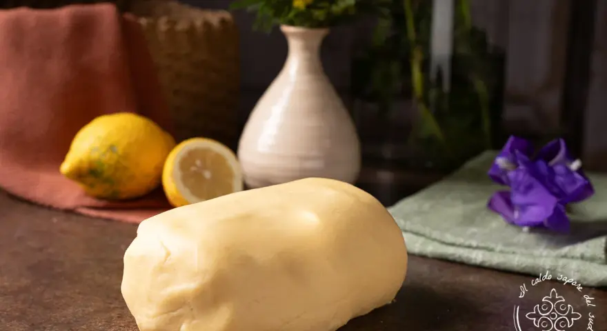 Impasto di pasta frolla che non si rompe, pronto per creare dolci perfetti. Accanto, limoni freschi e un tocco di colore.