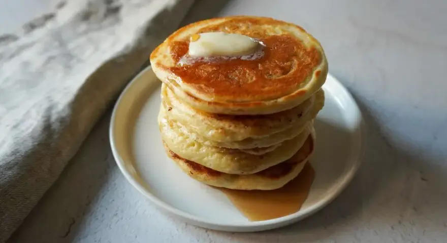 Pancakes dorati e soffici, impilati su un piatto bianco, con una noce di burro che si scioglie in cima e sciroppo d'acero che cola. Sembrano pronti per essere gustati, un vero piacere per gli occhi e per il palato, come un pancake in bottiglia pronto d...