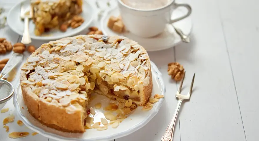 Torta con mandorle e zucchero a velo, perfetta per una ricetta frangipane. Accanto, una tazza di caffè e una fetta di torta.