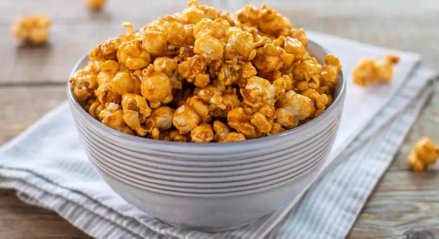 Una ciotola piena di pop corn caramellati, dorati e invitanti, su un tovagliolo a righe.