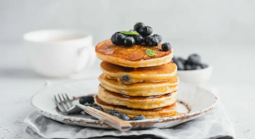 Pancake con farina di riso, guarniti con mirtilli freschi e sciroppo d'acero, su un piatto rustico con forchetta.