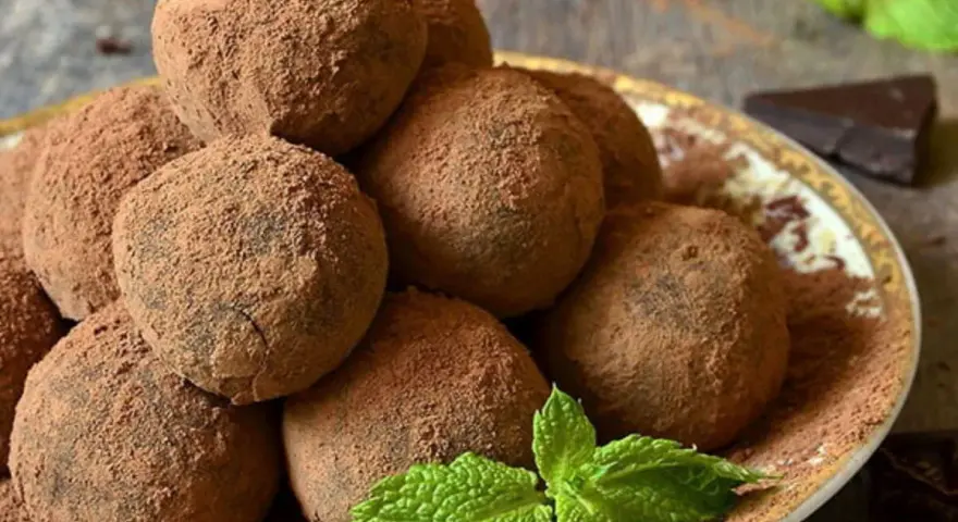Pile di tartufi al cioccolato facili e veloci, spolverati di cacao, con menta fresca e un pezzetto di cioccolato fondente.