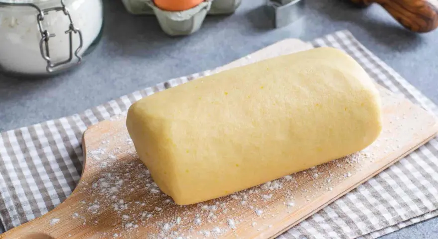 Rotolo di pasta frolla con strutto, pronto per essere trasformato in deliziosi biscotti. Ingredienti base visibili: farina, uova.