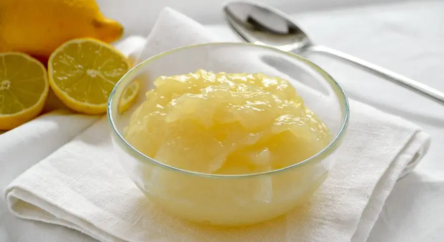 Una ciotola di deliziosa crema al limone senza uova, con limoni freschi affettati sullo sfondo.