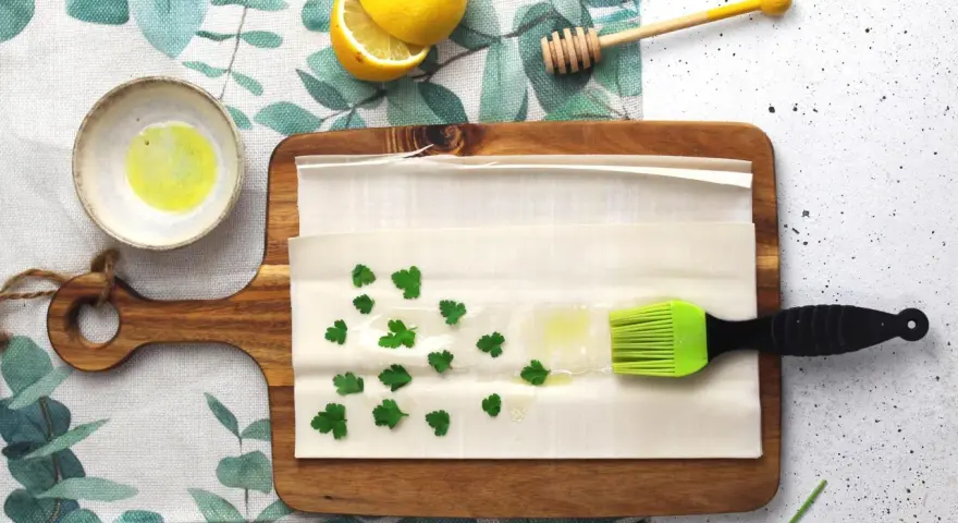 Preparazione per un piatto con pasta fillo: ingredienti come limone, miele, prezzemolo e olio su un tagliere.