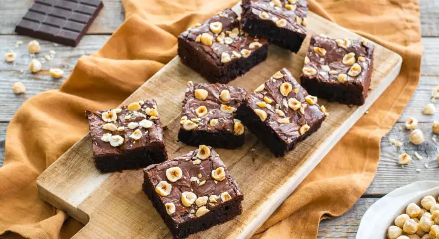 Deliziosi brownie senza glutine con nocciole tostate su tagliere di legno.