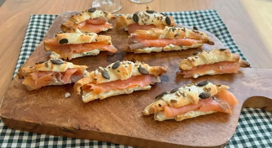 Cornetti di pasta sfoglia ripieni di salmone affumicato e formaggio cremoso, guarniti con semi.