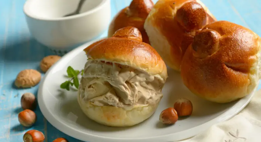 Brioches col tuppo, soffici e dorate, ripiene di gelato cremoso. Un dolce siciliano da gustare con nocciole e menta.