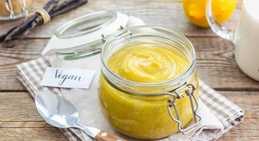 Crema pasticcera vegana in un barattolo di vetro, con bacche di vaniglia e limoni sullo sfondo.
