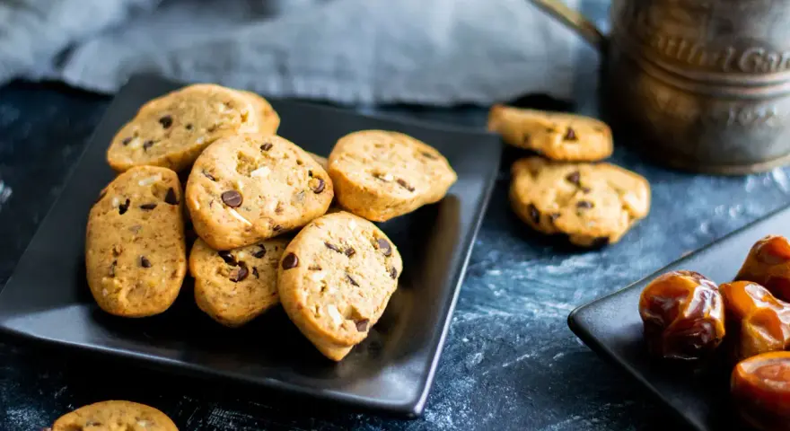 Biscotti vegan con gocce di cioccolato e datteri su piatti neri, pronti per una pausa golosa.