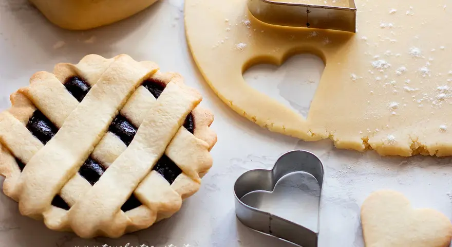 Una crostata con ripieno di marmellata, pasta frolla stesa e tagliabiscotti a forma di cuore.