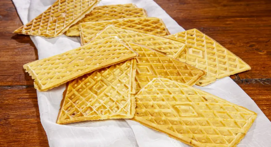 Un mucchio di croccanti ferratelle abruzzesi, dolci tradizionali, disposte su un panno bianco su un tavolo di legno.