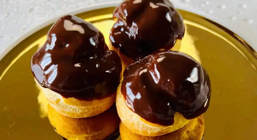 Tre golosi bignè al cioccolato, lucidi e invitanti, su un piatto dorato.