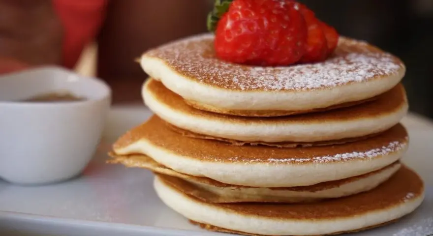 Pancake Bimby perfetti, impilati e spolverati di zucchero a velo, con una fragola fresca in cima.