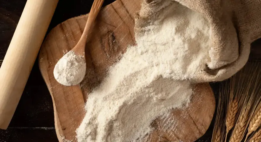 Farina 0 al posto della 00 nei dolci: un sacco di farina, un mestolo e spighe di grano su un tagliere di legno.