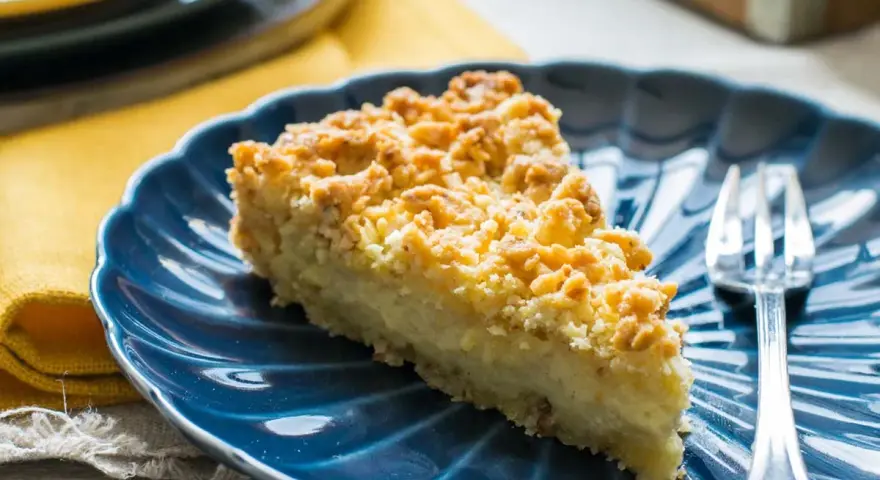 Fetta di sbrisolona con crema pasticcera su piatto blu, con forchetta trasparente.