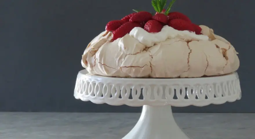 Pavlova ricetta: meringa croccante fuori e morbida dentro, guarnita con panna montata e fragole fresche.
