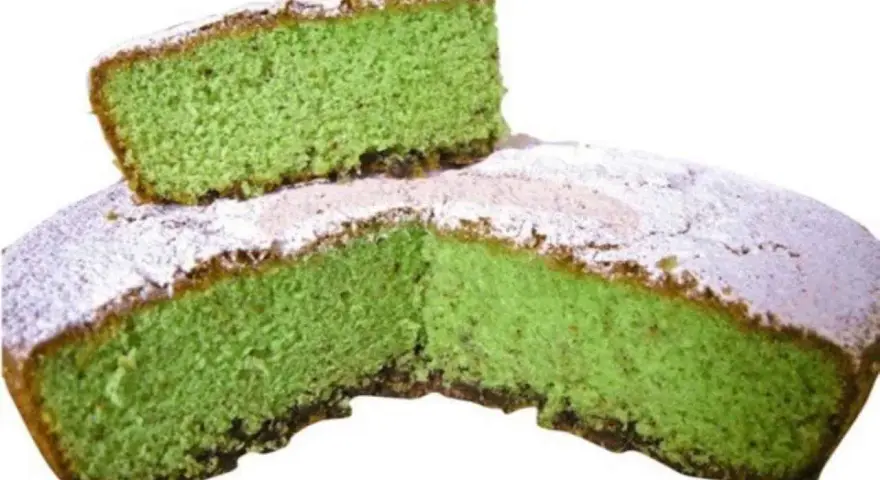Una fetta di torta alla menta verde brillante, cosparsa di zucchero a velo, è appoggiata su una torta intera.