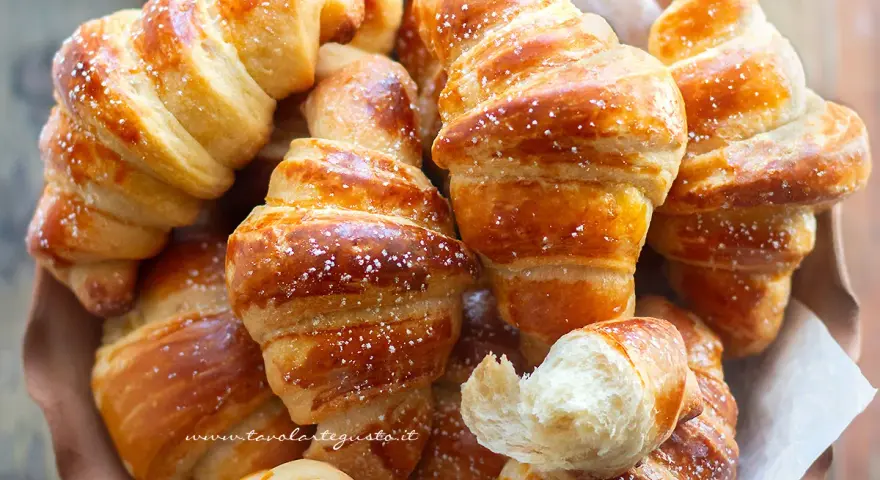Brioches fatte in casa, dorate e soffici, cosparse di zucchero a velo. Un profumo invitante che ricorda la colazione perfetta.
