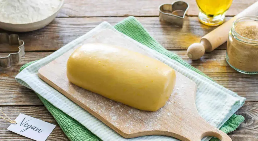 Impasto giallo pronto per biscotti, con un'etichetta "Vegan" e ingredienti come farina, zucchero e olio.
