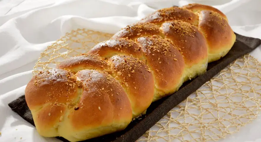 Treccia dorata di dolci con farina manitoba, cosparsa di granella croccante, su un letto di lino bianco.
