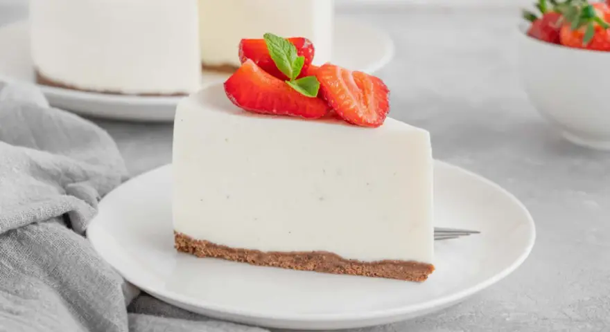 Una fetta di torta fredda allo yogurt senza biscotti, guarnita con fragole fresche e menta, su un piatto bianco.