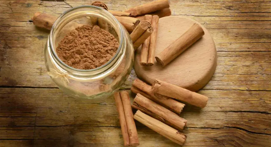 Barattolo di cannella in polvere e bastoncini su un tagliere di legno. Ingredienti essenziali per la cucina.