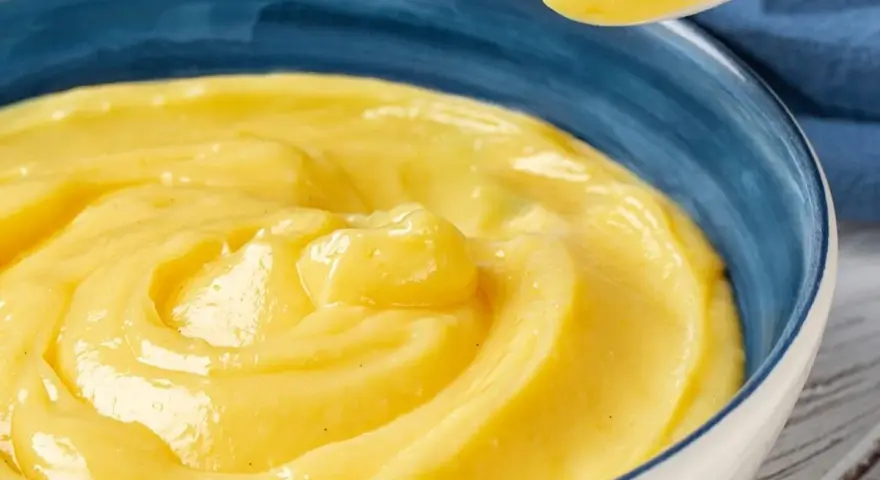 Una ciotola blu piena di deliziosa crema pasticcera senza uova, con un cucchiaio che ne preleva una porzione.