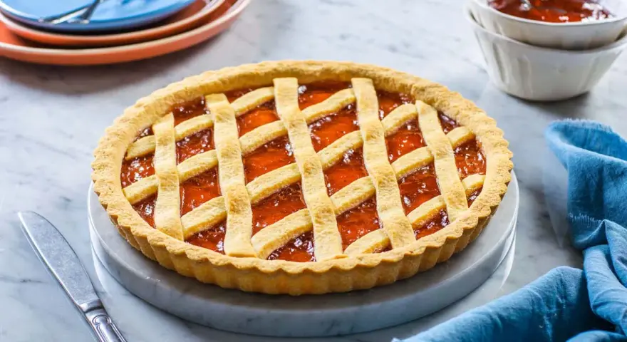 Crostata alla marmellata dorata, perfetta per il tempo cottura crostata forno statico. Servita su un piatto di marmo con tovagliolo blu.