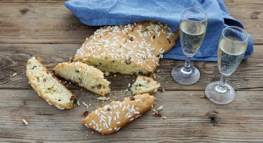 Fette di ciambella romagnola, cosparse di zuccherini, accanto a due bicchieri di spumante.