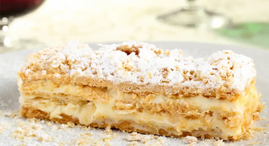 Una fetta di rettangolare torta millefoglie compleanno, con crema pasticcera e zucchero a velo.