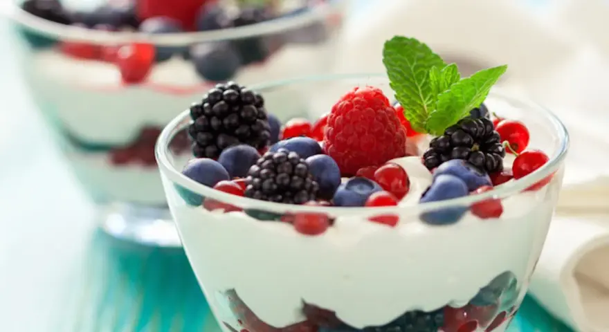 Deliziosa mousse allo yogurt con frutti di bosco freschi e una fogliolina di menta, servita in coppette di vetro.
