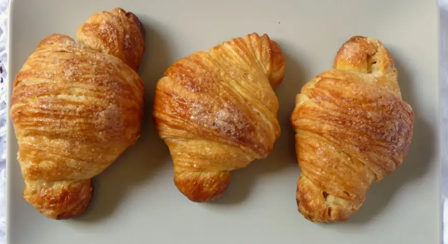 Tre deliziosi croissant dorati, cosparsi di zucchero, disposti su un piatto grigio.