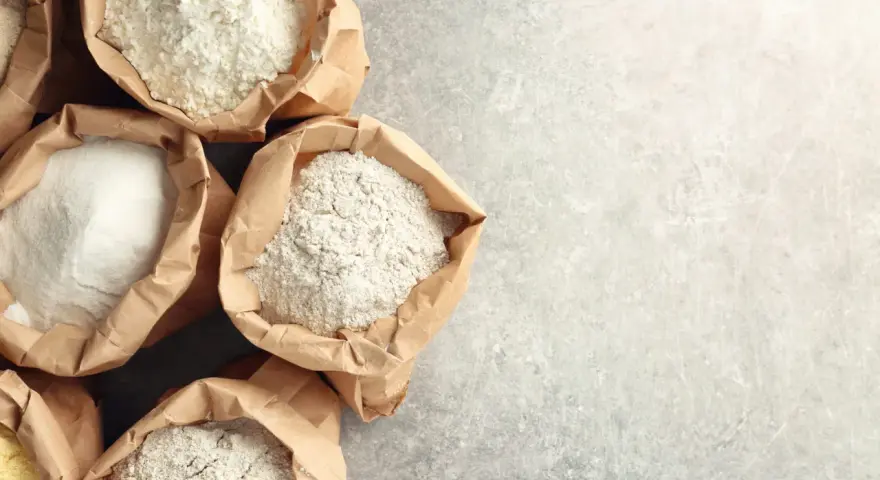 Sacchetti di carta aperti pieni di diverse farine, tra cui farina 0 e manitoba, pronte per creare pane e dolci.