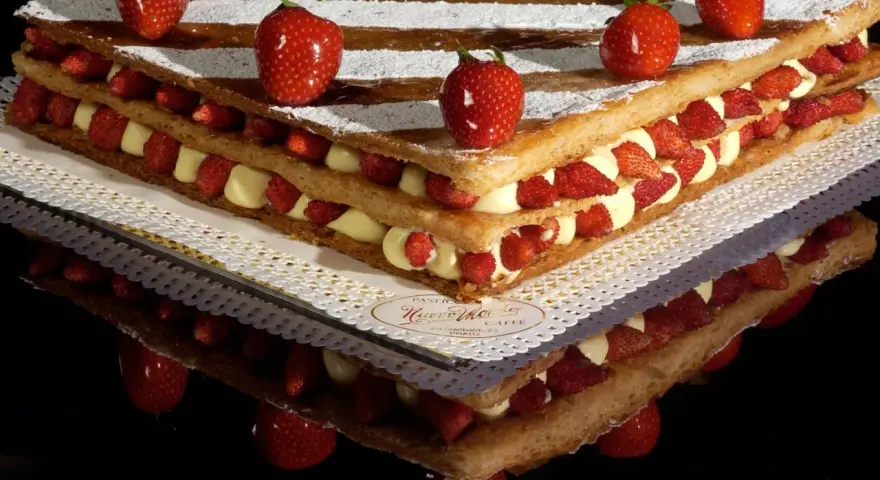 Un invitante millefoglie cake con strati di crema pasticcera e fragole fresche, decorato con fragole intere e zucchero a velo.