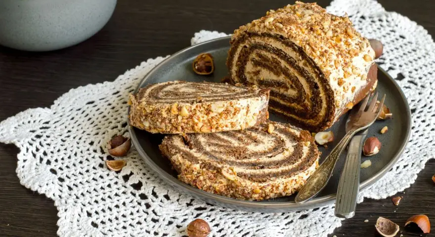 Rotolo alla Nutella ricoperto di granella di nocciole, servito su un piatto con due fette tagliate.
