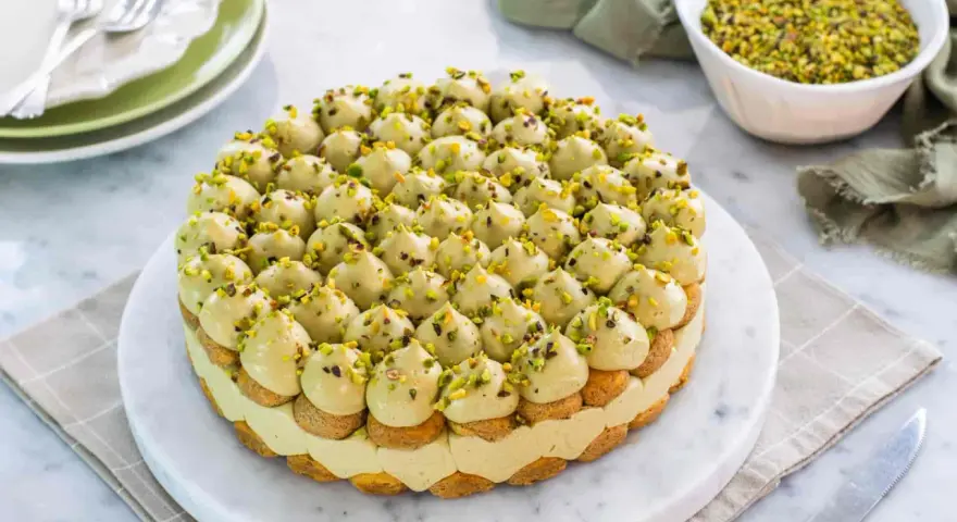 Torta rotonda con tante piccole meringhe verdi, guarnite con granella di pistacchio. Un delizioso tiramisù al pistacchio pronto per essere gustato.