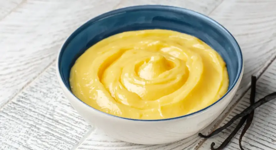 Una ciotola di crema gialla, liscia e invitante, con baccelli di vaniglia accanto. Perfetta per ogni ricetta crema.