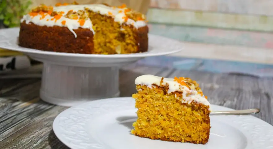 Una fetta di torta di carote senza glutine, soffice e profumata, con glassa bianca e decorazioni arancioni.