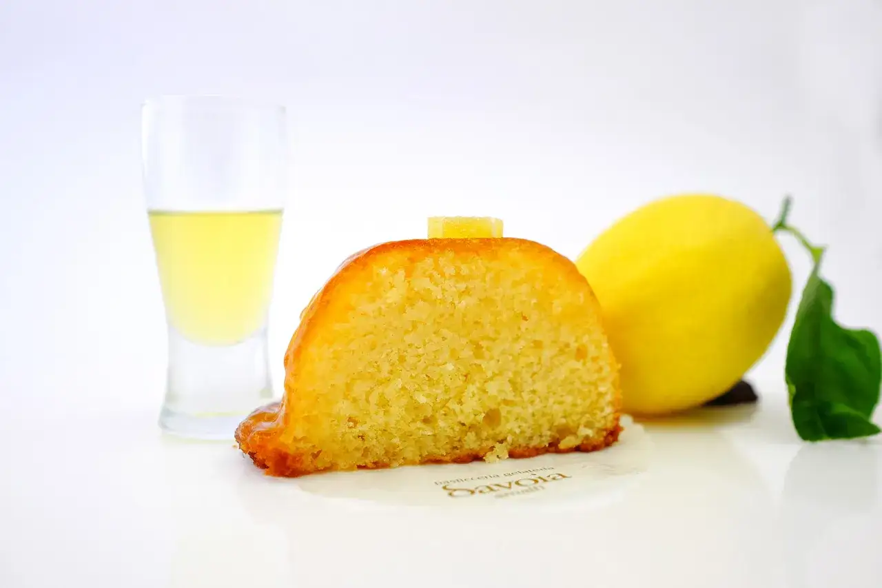 Deliziosi dolci con eritritolo, una fetta di torta al limone con un bicchierino di liquore e un limone fresco.