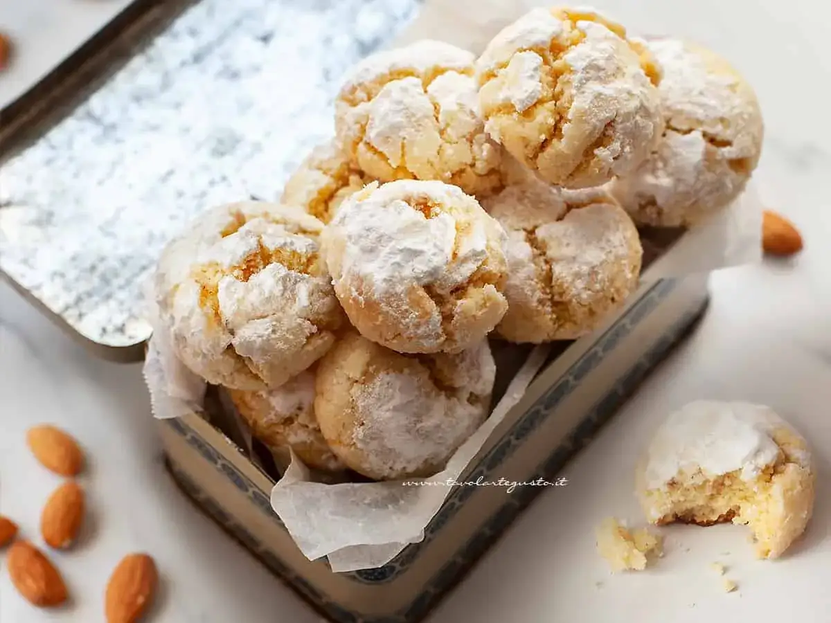 Biscotti senza zucchero, friabili e ricoperti di zucchero a velo, invitano a un morso goloso. Mandorle sparse completano la scena.