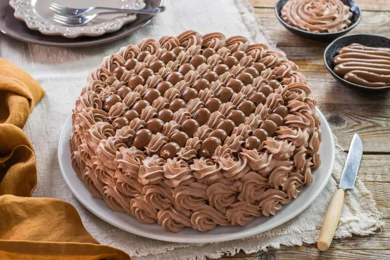 Torta decorata con riccioli di crema pasticcera al cioccolato e palline di cioccolato.