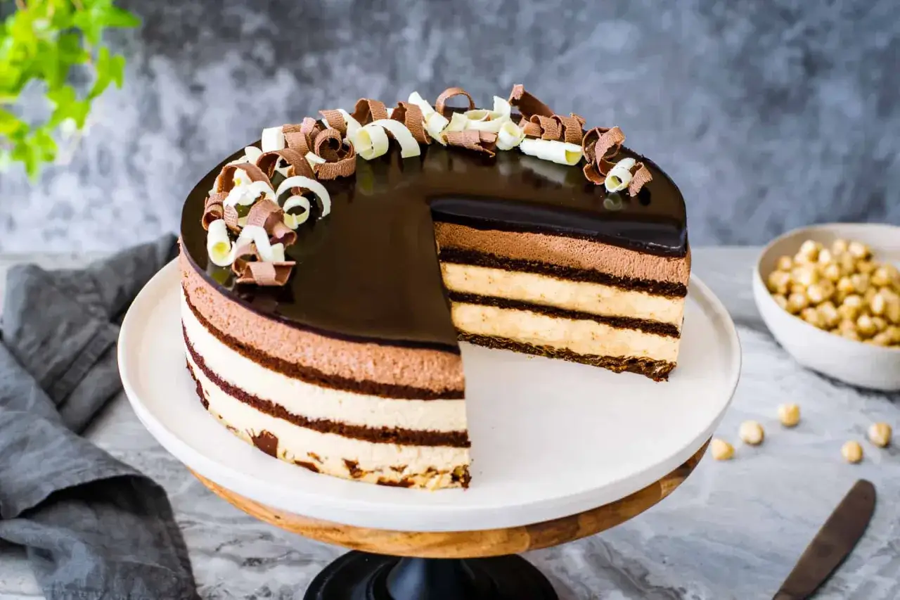 Una golosa torta sette veli, con strati di mousse al cioccolato e crema, lucida e decorata con riccioli di cioccolato bianco e fondente.