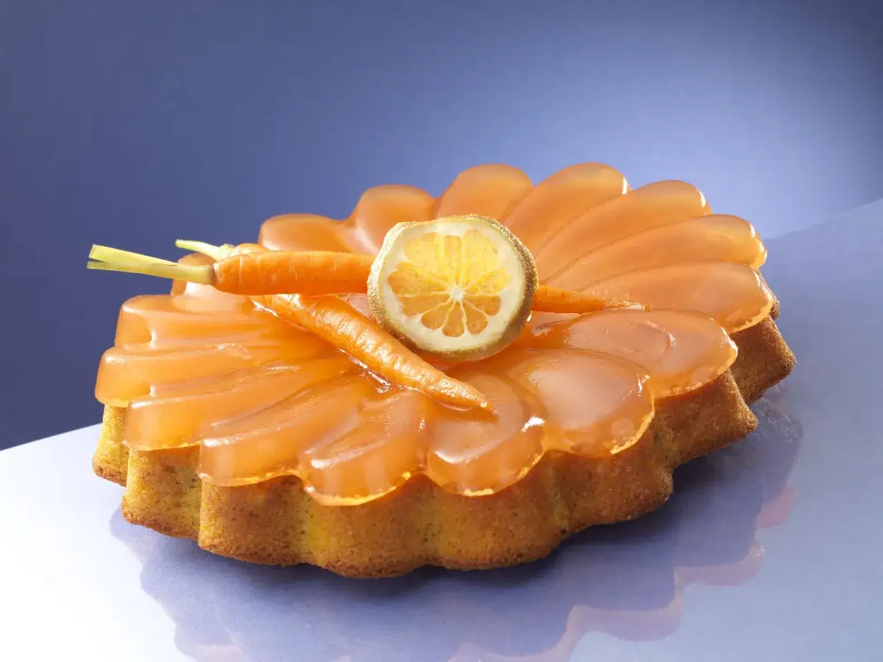 Deliziosa torta di carote con glassa arancione, decorata con carotine e una fetta di agrume essiccato.