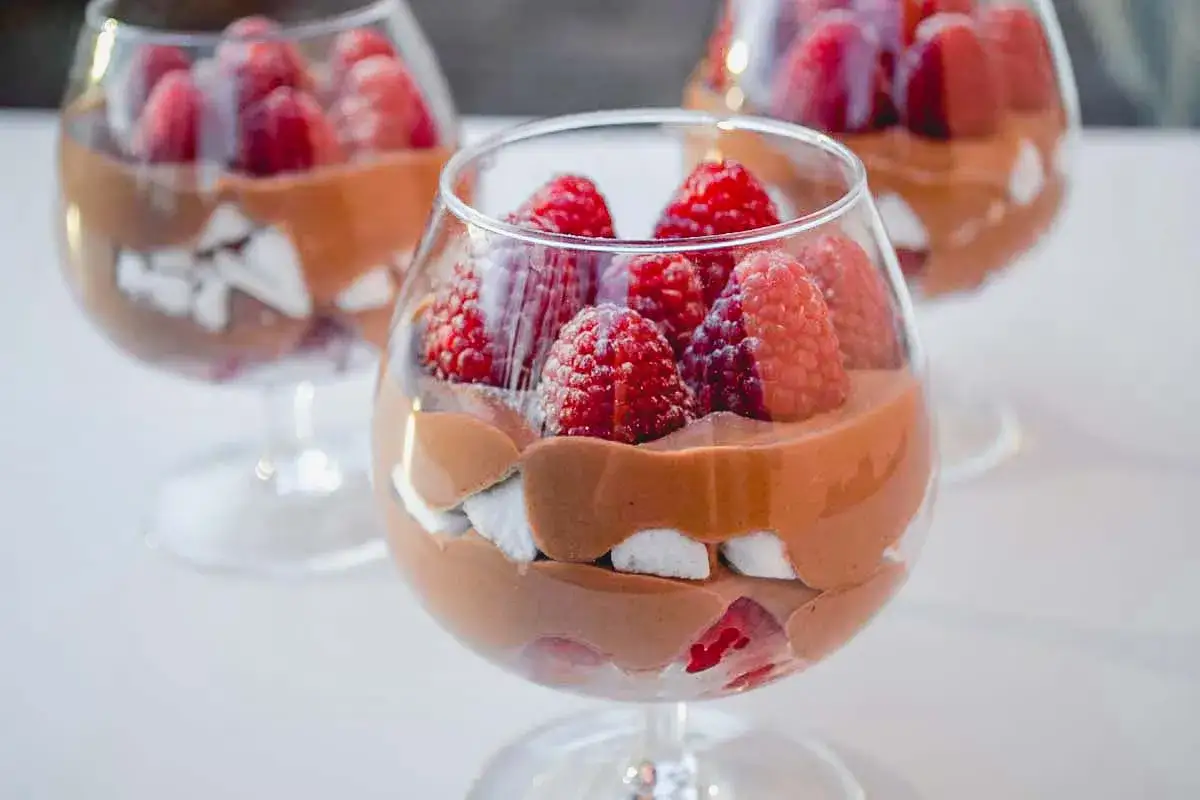 Deliziosa mousse al cioccolato con lamponi freschi e pezzi di meringa in coppe di vetro.